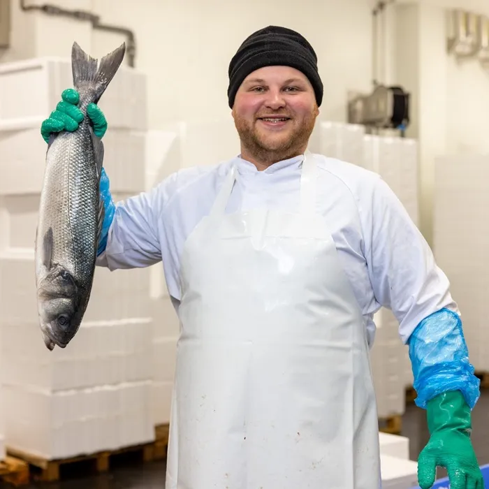 werknemer staat in een gekoelde ruimte van een visleverancier aan horeca met een vis in zijn handen